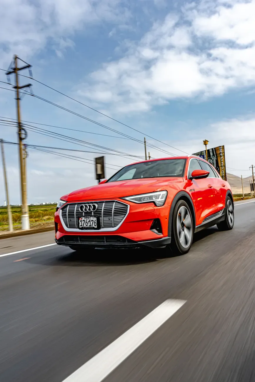 A striking red Audi E-Tron driving on an open rural road under a blue sky.