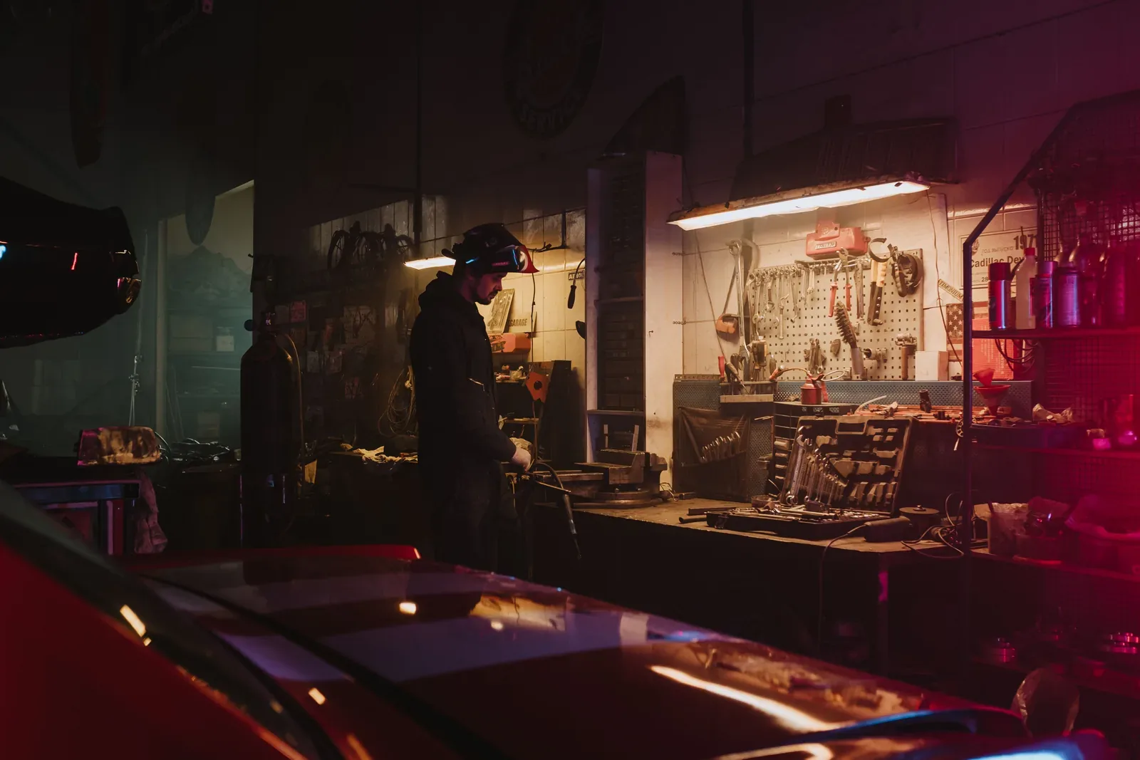 Mechanic working in a dimly lit garage workshop surrounded by tools and equipment.
